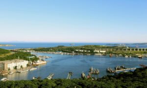 Во Владивостоке разгорается юридический спор вокруг бухты Улисс, которая была передана в собственность Военно-морского флота (ВМФ) по решению суда. Местные предприниматели, ведущие бизнес на этой территории с начала 2000-х годов, оспаривают это решение, утверждая, что суд опирался на документы почти вековой давности. Бухта Улисс, расположенная рядом с мостом на остров Русский, является важной промышленной гаванью, где также базируются корабли Тихоокеанского флота. В прошлом году Генпрокуратура добилась передачи территории в пользование Минобороны, что поставило местный бизнес в сложное положение. Предприниматели лишились земли и инвестиций без компенсации. Согласно иску Генпрокуратуры, бухта изначально предназначалась для нужд обороны, а сделки по её продаже в 1990-х годах были признаны недействительными. Главным доказательством в суде стали справки о передаче территории военным частям в 1930-х годах. Однако ответчики утверждают, что эти документы не имеют юридической силы, так как в них отсутствуют чёткие границы и кадастровые данные. На данный момент четыре компании уже лишились своих активов без компенсации, а ещё 19 находятся в зоне риска. Предприниматели требуют пересмотра дела и учёта официального документа о высвобождении земель из владения Минобороны, который суд отказался приобщить к делу.. Владивосток, бухта Улисс, ВМФ, Генпрокуратура, бизнес